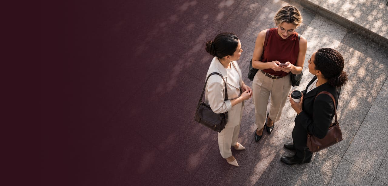 Three colleagues talking together on a sunlit plaza, one checking her phone