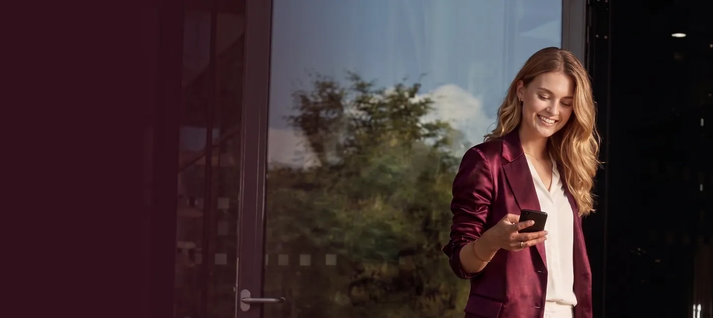 A woman in a burgundy blazer smiling at her phone