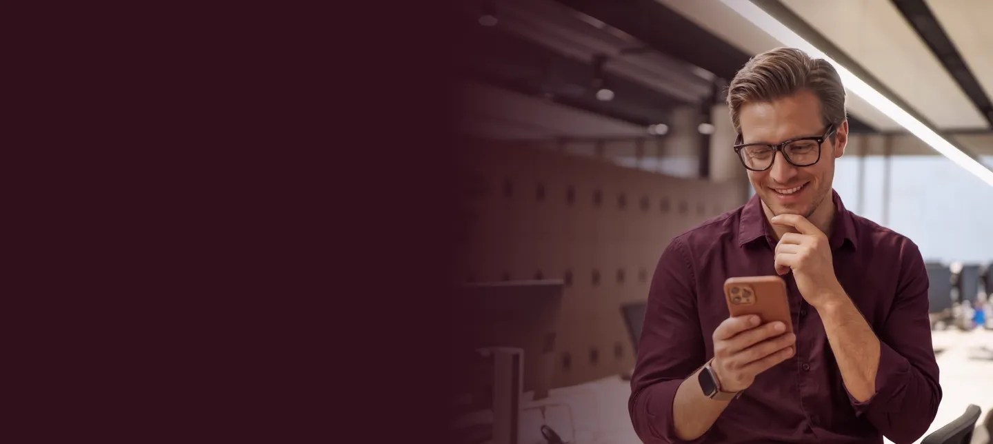 A smiling man in glasses looking at his phone in an office