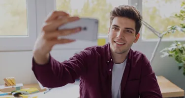 A man taking a selfie with his phone at his desk